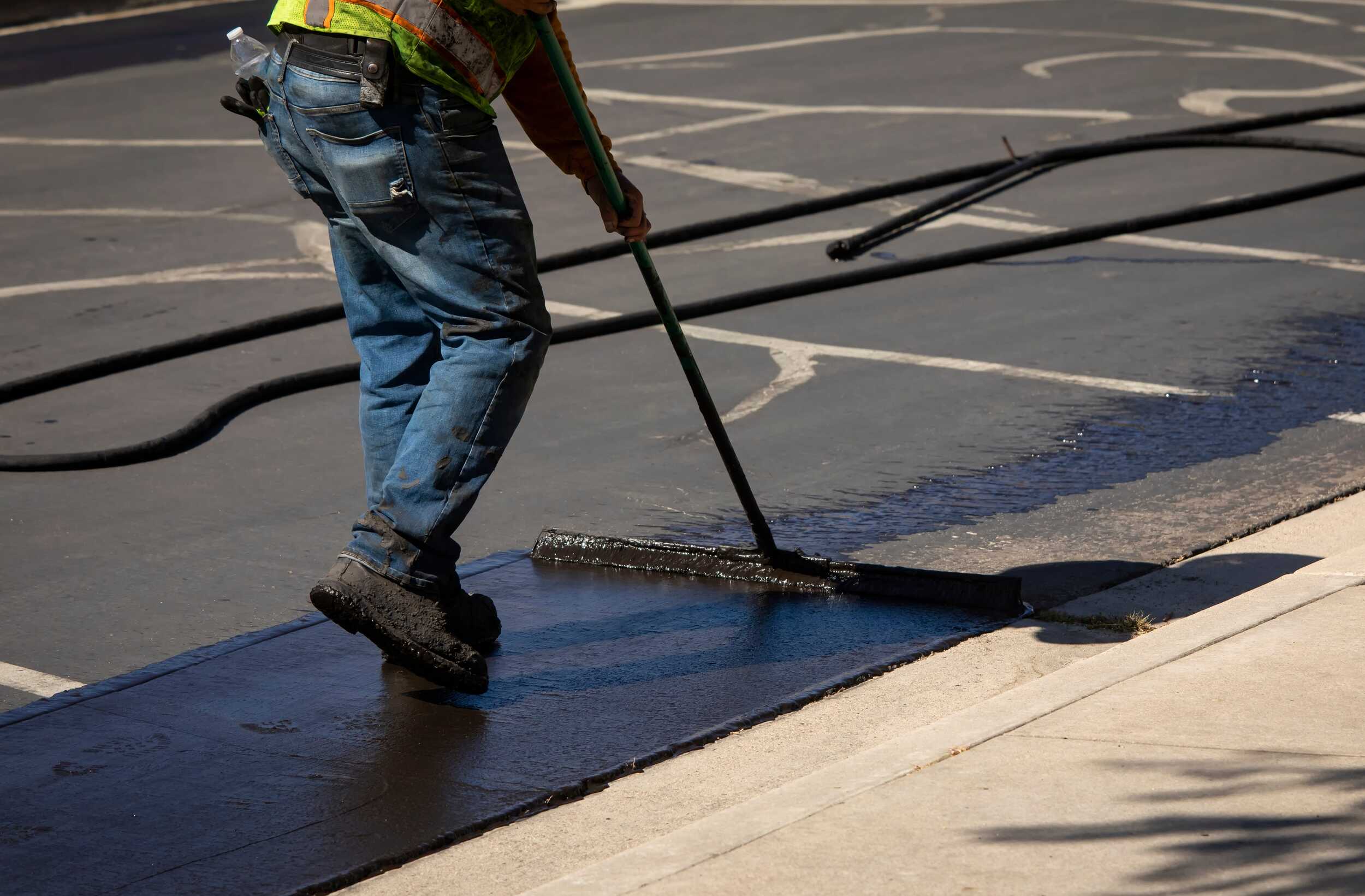 Worker squeegees new sealcoat during an asphalt maintenance job.